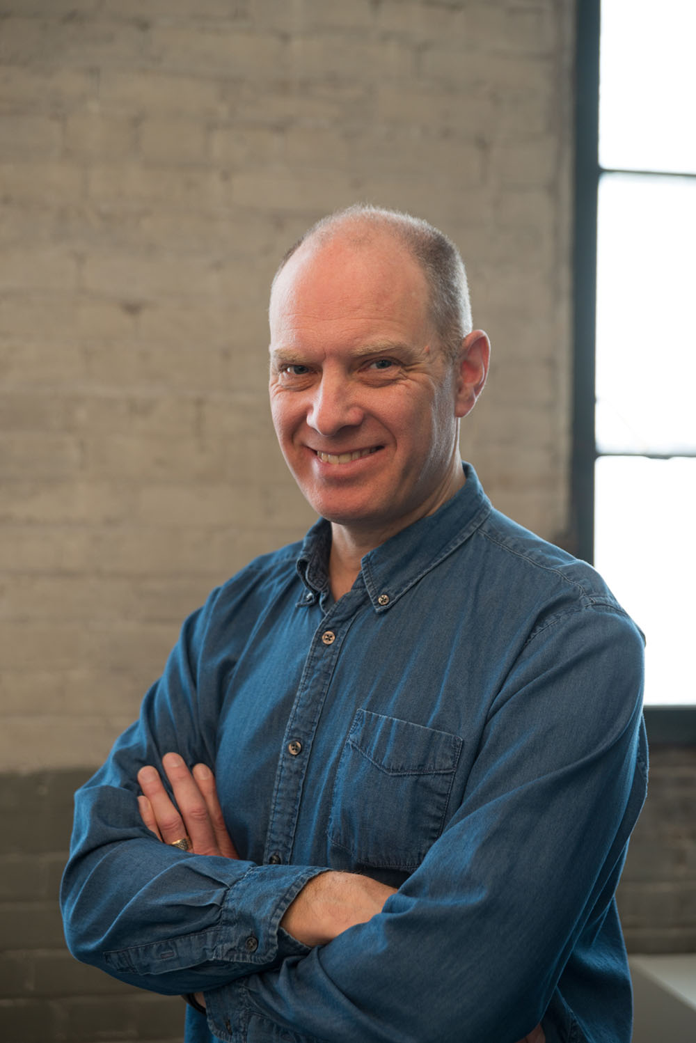 David Jón Fuller posing with folded arms in front of a weathered brick wall.